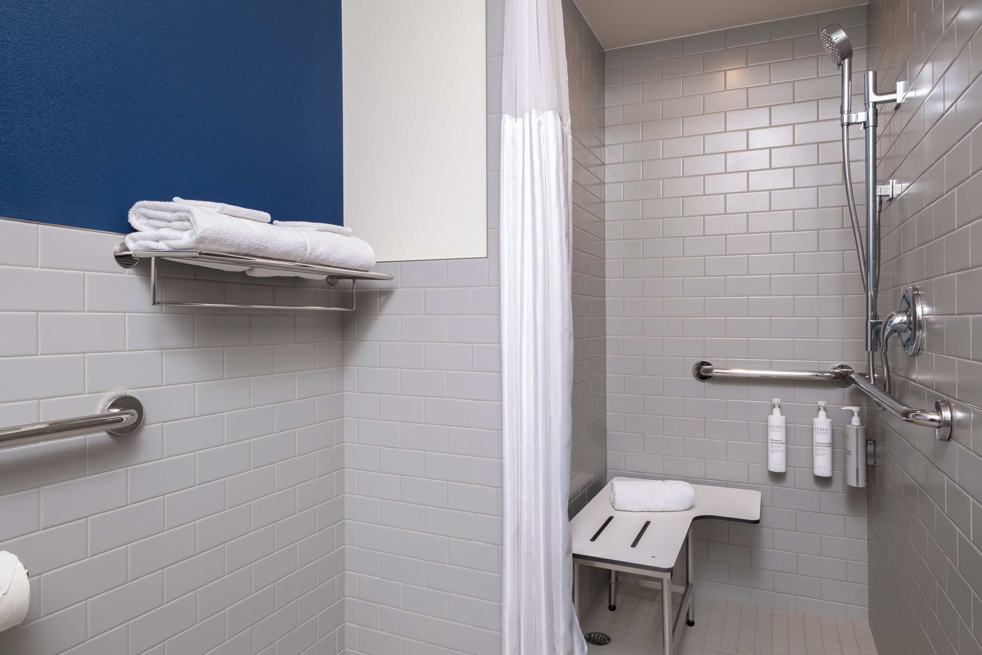 A modern bathroom with grey tiled walls, a white sink, and a shower with a handheld showerhead.