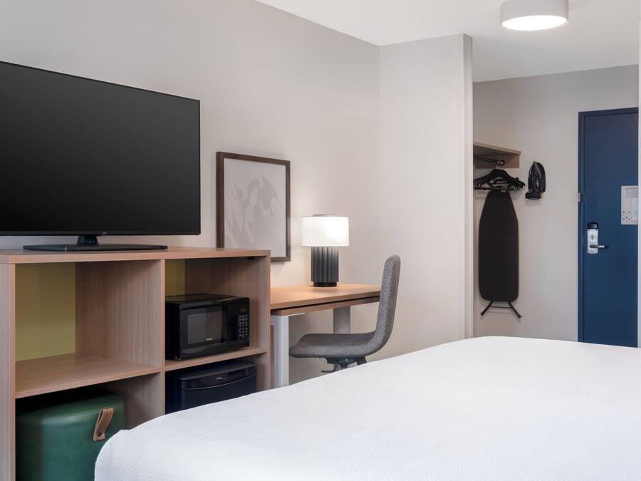 A hotel room with a bed, a desk with a computer, a television, a microwave, and a lamp.