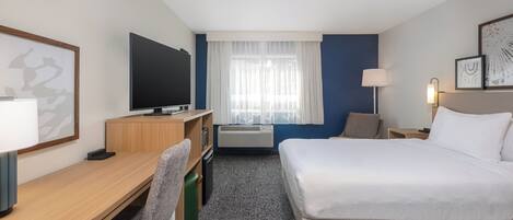 A hotel room with a bed, desk, chair, TV, and a window with curtains.