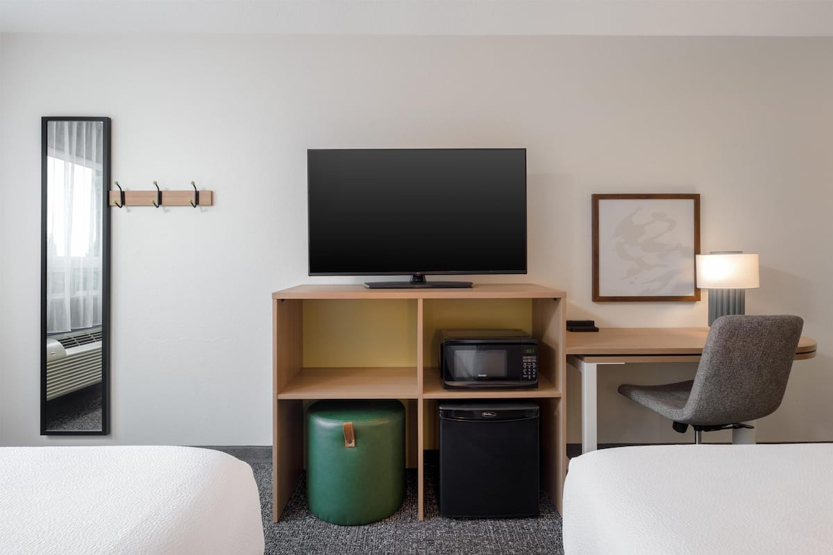 Una habitación de hotel con televisor, microondas, refrigerador pequeño y un cubo de basura verde.