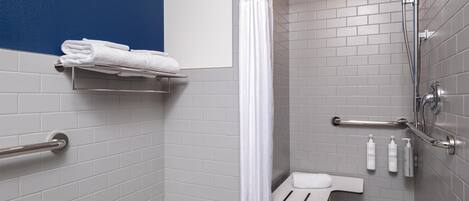 A modern bathroom with grey tiles, a white sink, a shower with a handheld showerhead, and a towel rack.