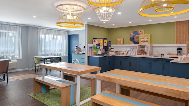 Une cuisine moderne avec des armoires bleues, un plan de travail sur lequel sont disposés divers aliments, et un coin repas avec des tables et des bancs en bois.