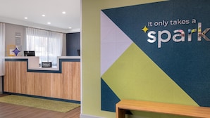 Un espace d’accueil d’hôtel au design moderne, agrémenté d’une œuvre d’art murale aux motifs géométriques et d’un comptoir d’accueil en bois.