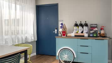 Une chambre avec une porte bleue, un coin cuisine équipé d’un espace pour préparer le café et une table accessible aux personnes en fauteuil roulant.