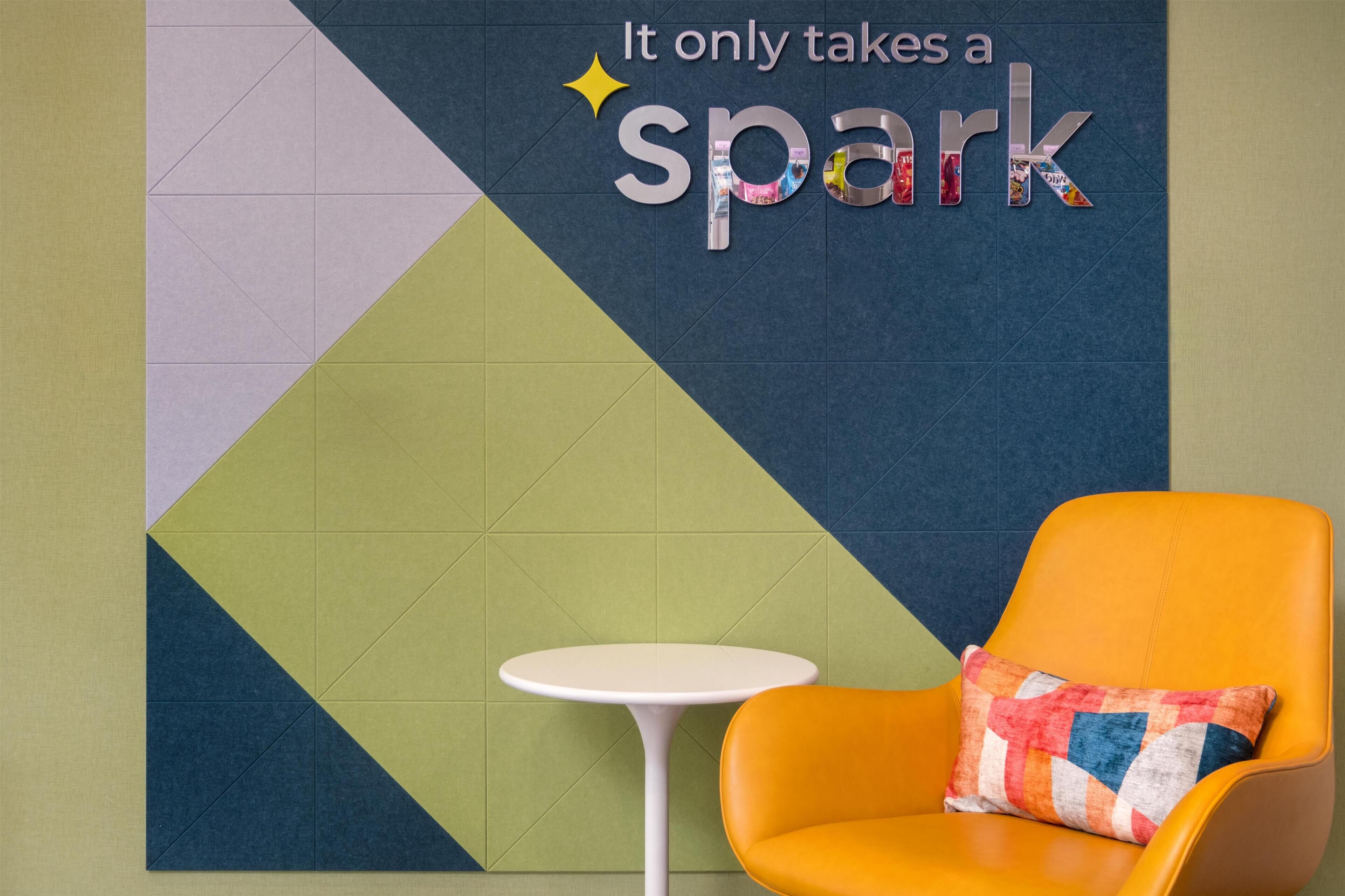 A room with a geometric patterned wall, a small white table, and an orange chair with a colorful cushion.