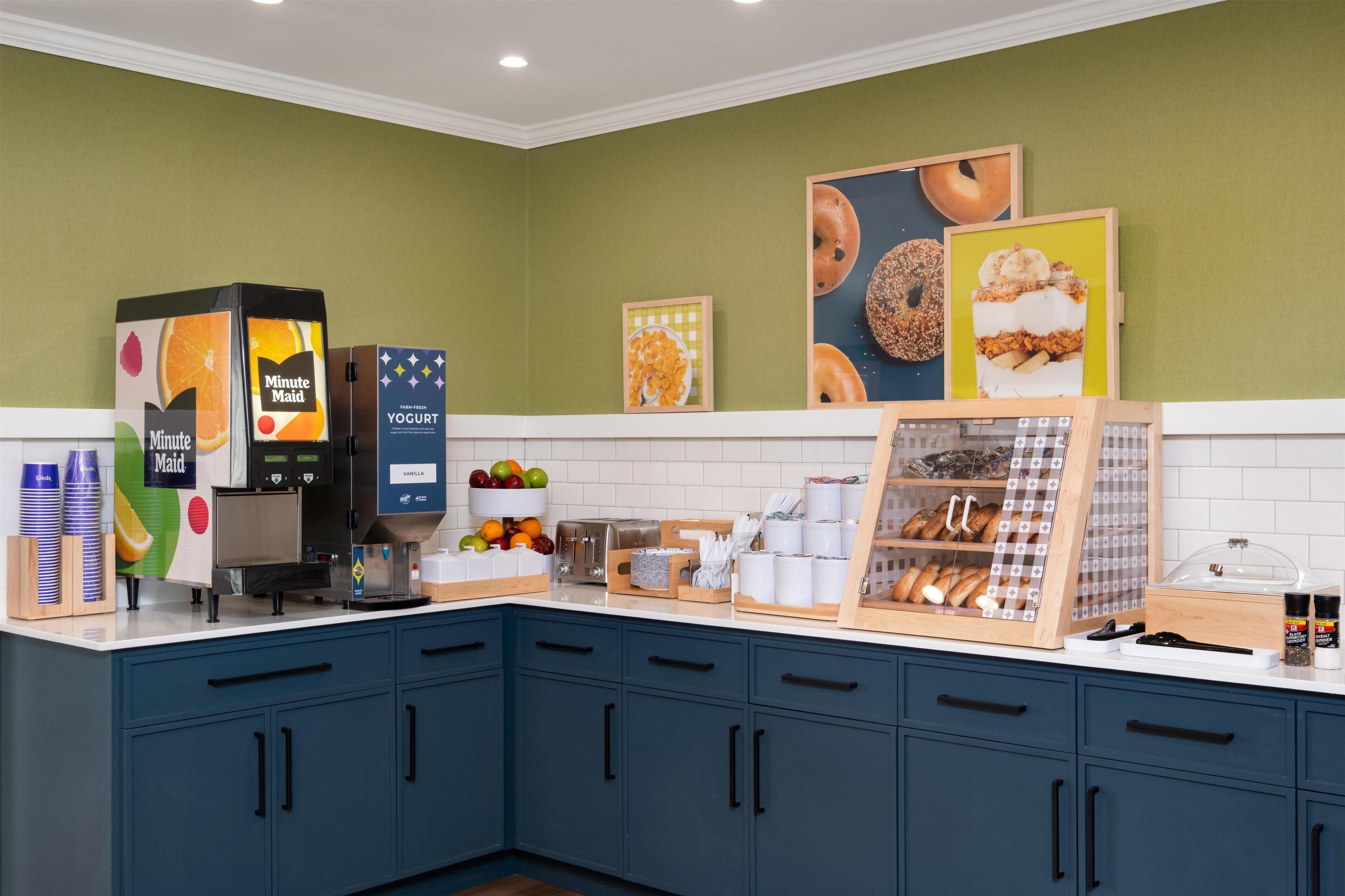 A kitchen area with a coffee machine, a yogurt dispenser, and a display of bread and pastries.