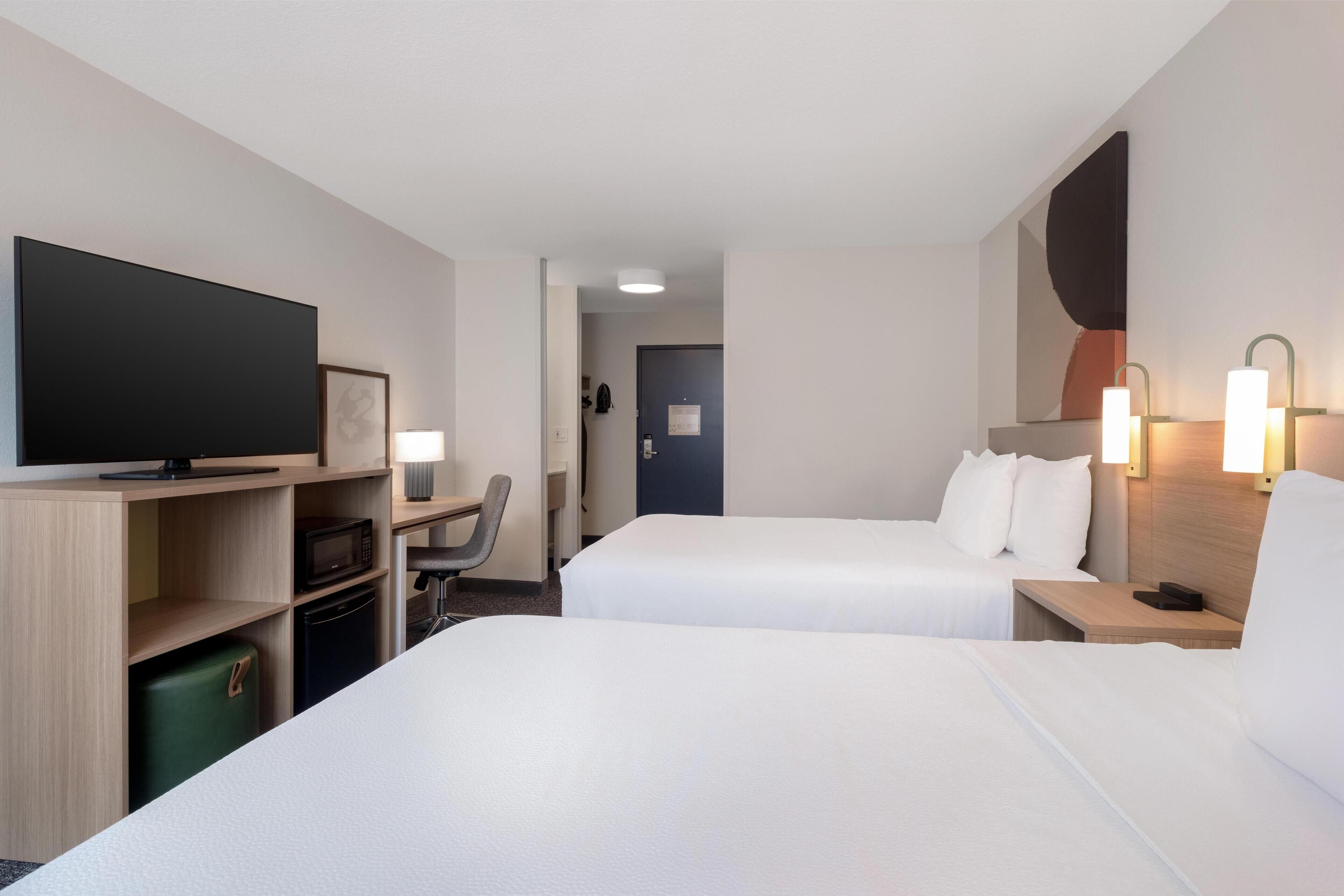 A hotel room with two beds, a TV, a desk with a chair, and a microwave.