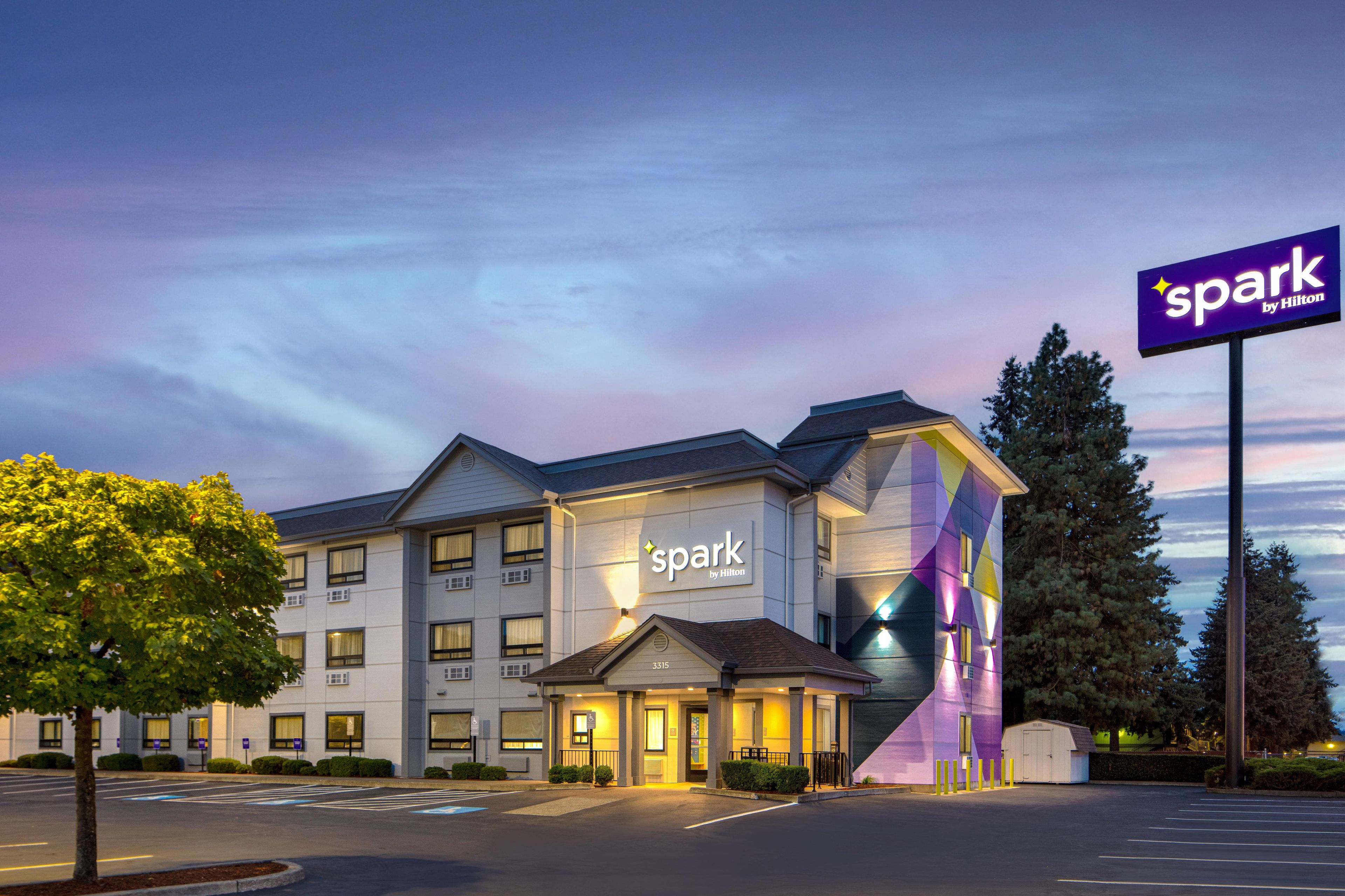 A hotel with a modern design, featuring a prominent 'spark by Hilton' sign, a well-lit entrance, and a parking lot.