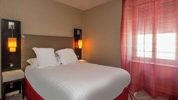 A hotel room with a large bed, two bedside lamps, a nightstand, and a window with sheer curtains.