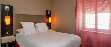 A hotel room with a large bed, two bedside lamps, a nightstand, and a window with sheer curtains.