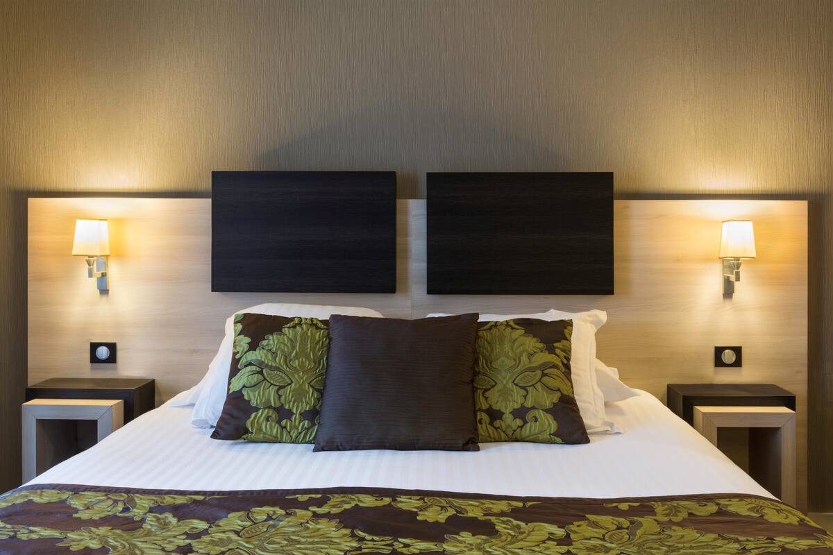 A hotel room with a large bed, two wall-mounted lamps, and a decorative headboard.