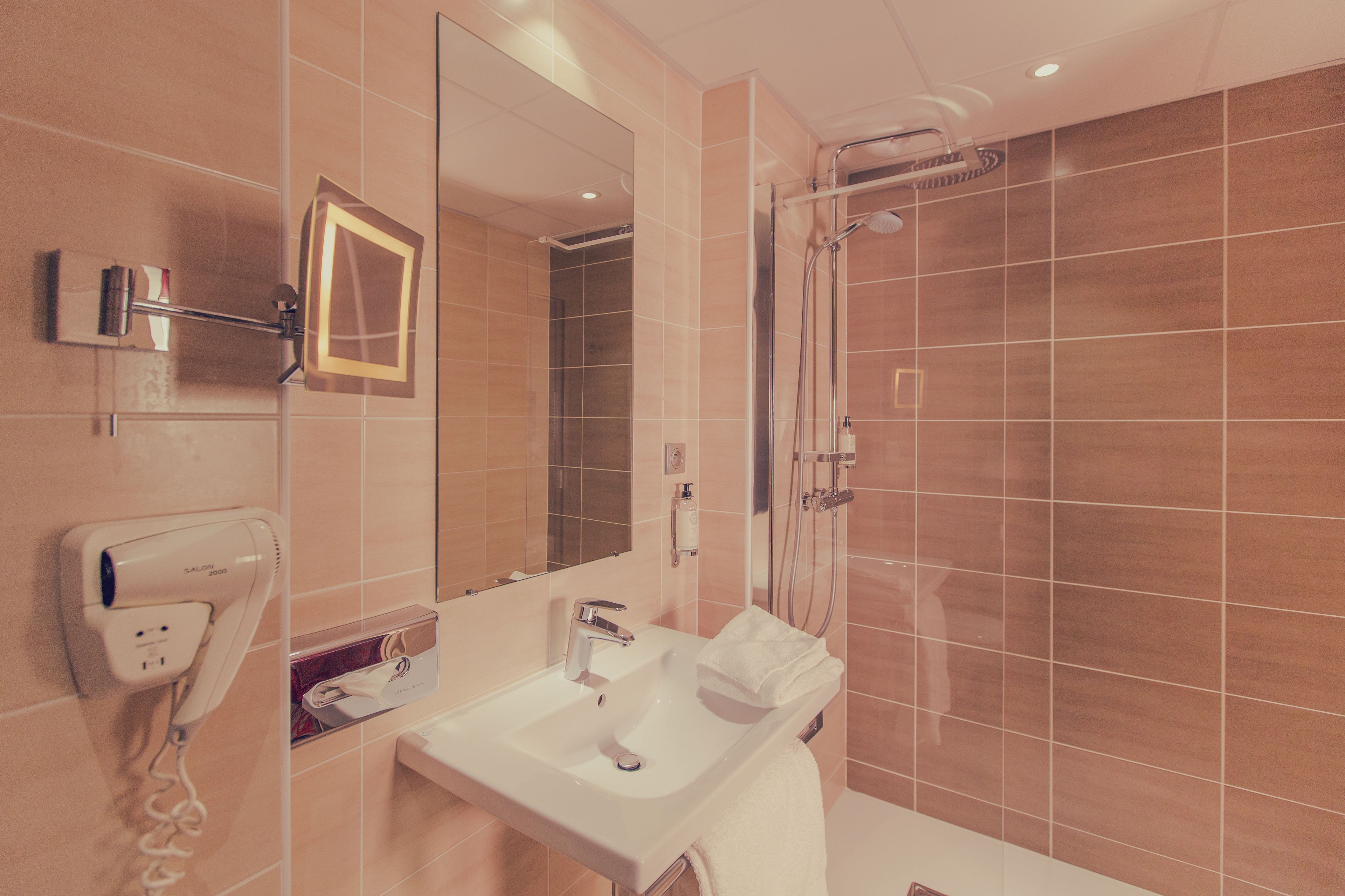 A bathroom with a sink, mirror, hairdryer, and shower.