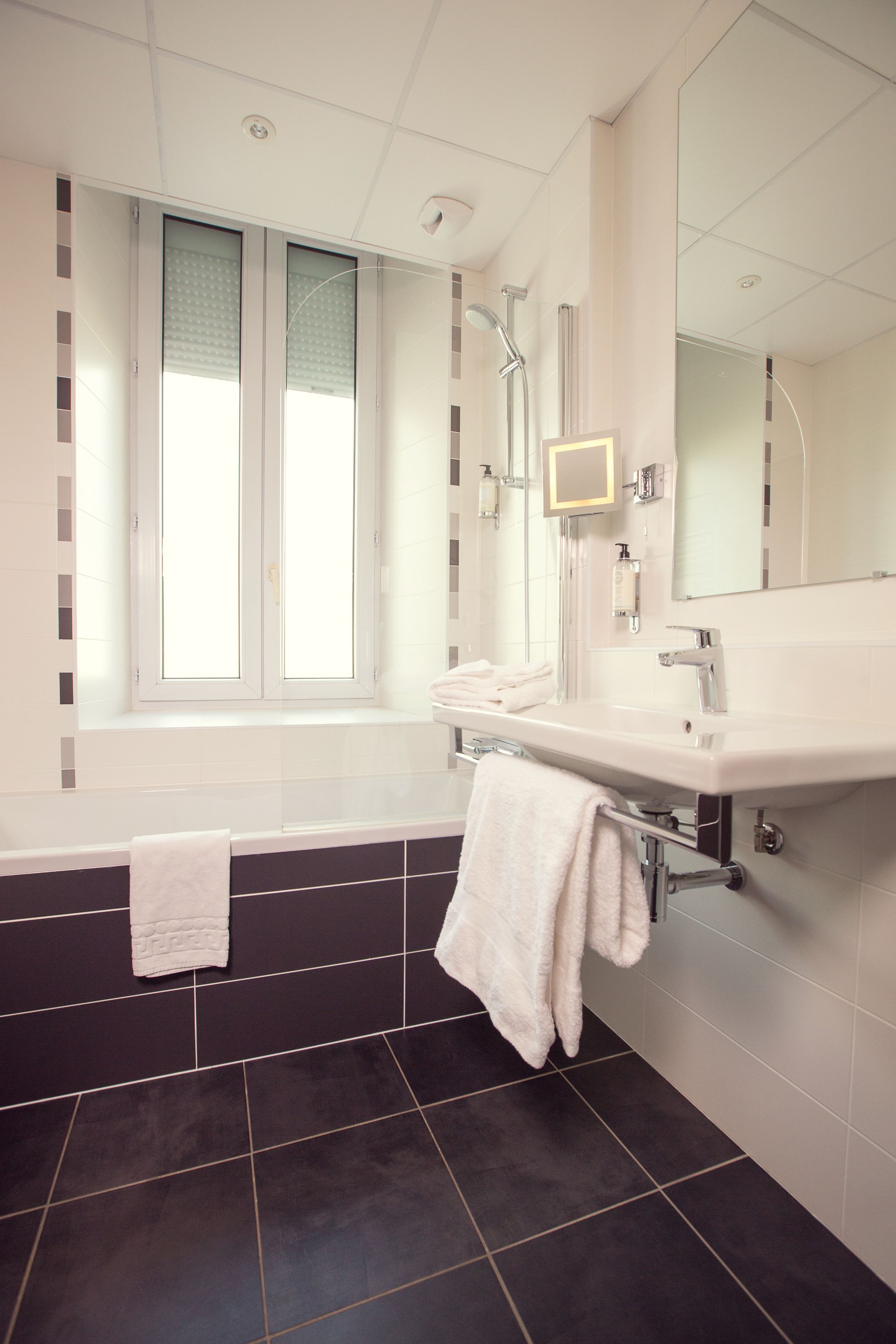 A modern bathroom with a bathtub, a large mirror, and a window.