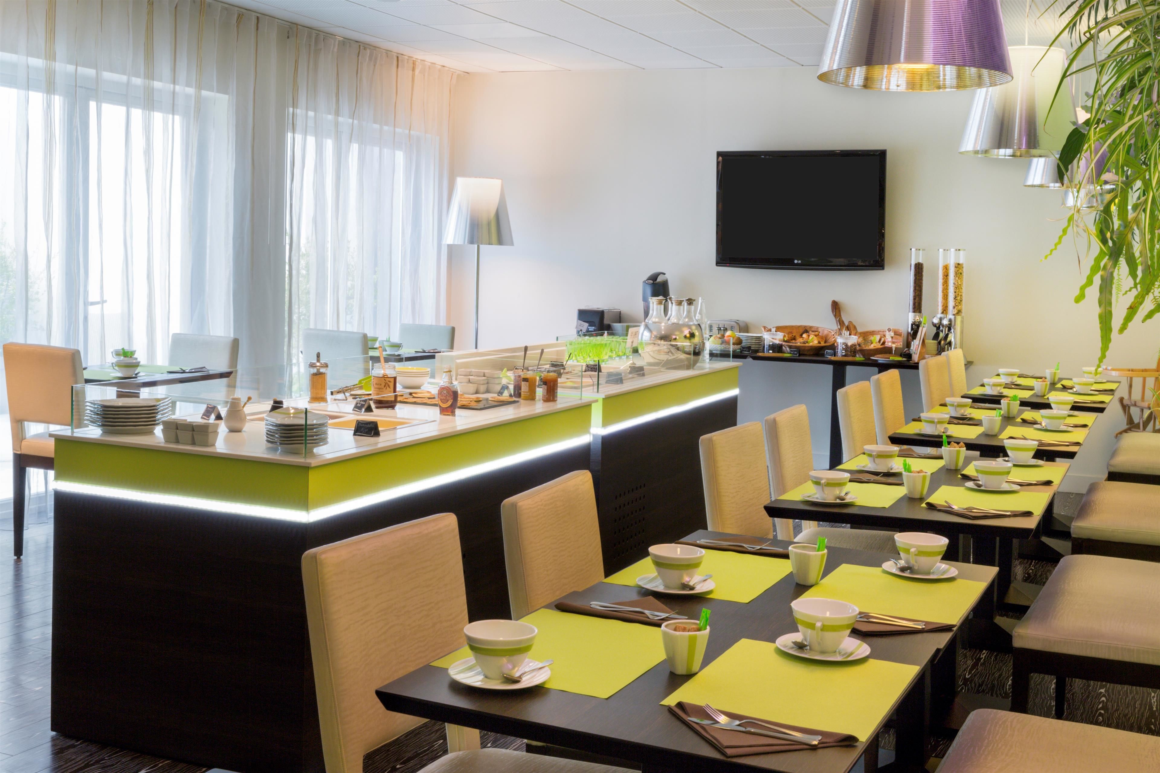 Uma área de refeições moderna com uma mesa comprida posta para uma refeição, um espaço de bar com balcão e uma televisão fixada na parede.