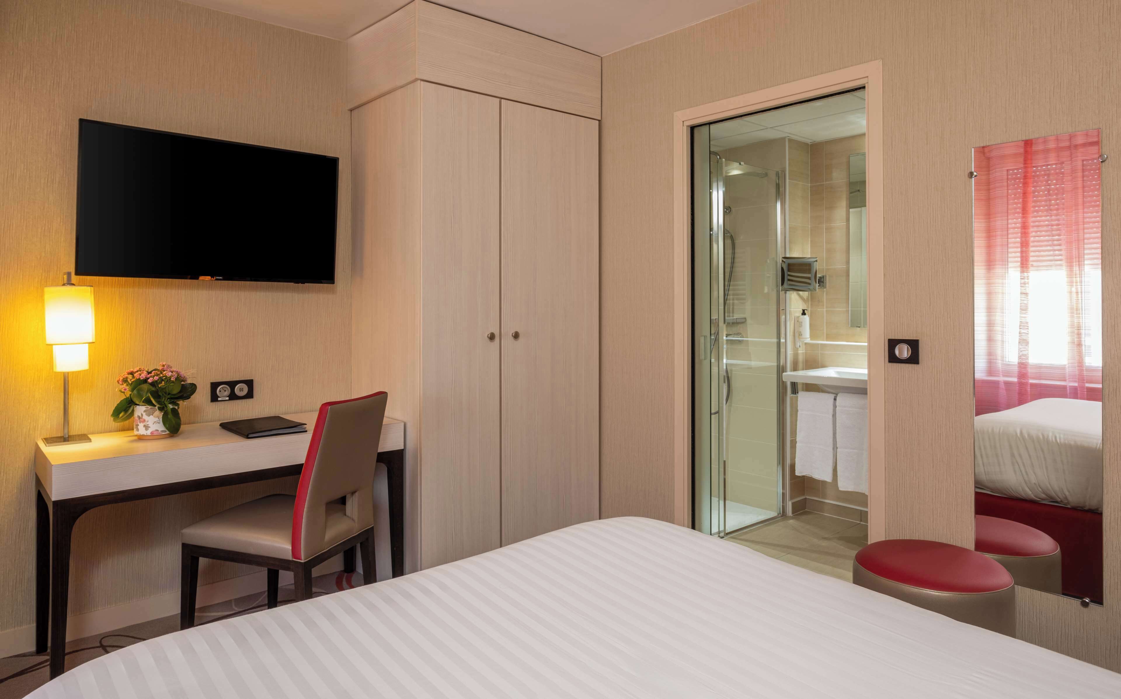 Habitación de hotel con cama, escritorio con silla, televisor, zona de ducha y baño.