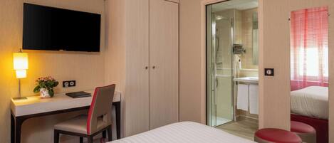 Habitación de hotel con cama, escritorio con silla, televisor, zona de ducha y baño.