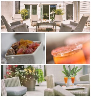 A patio with wicker furniture, a table with drinks, and a view of the house.