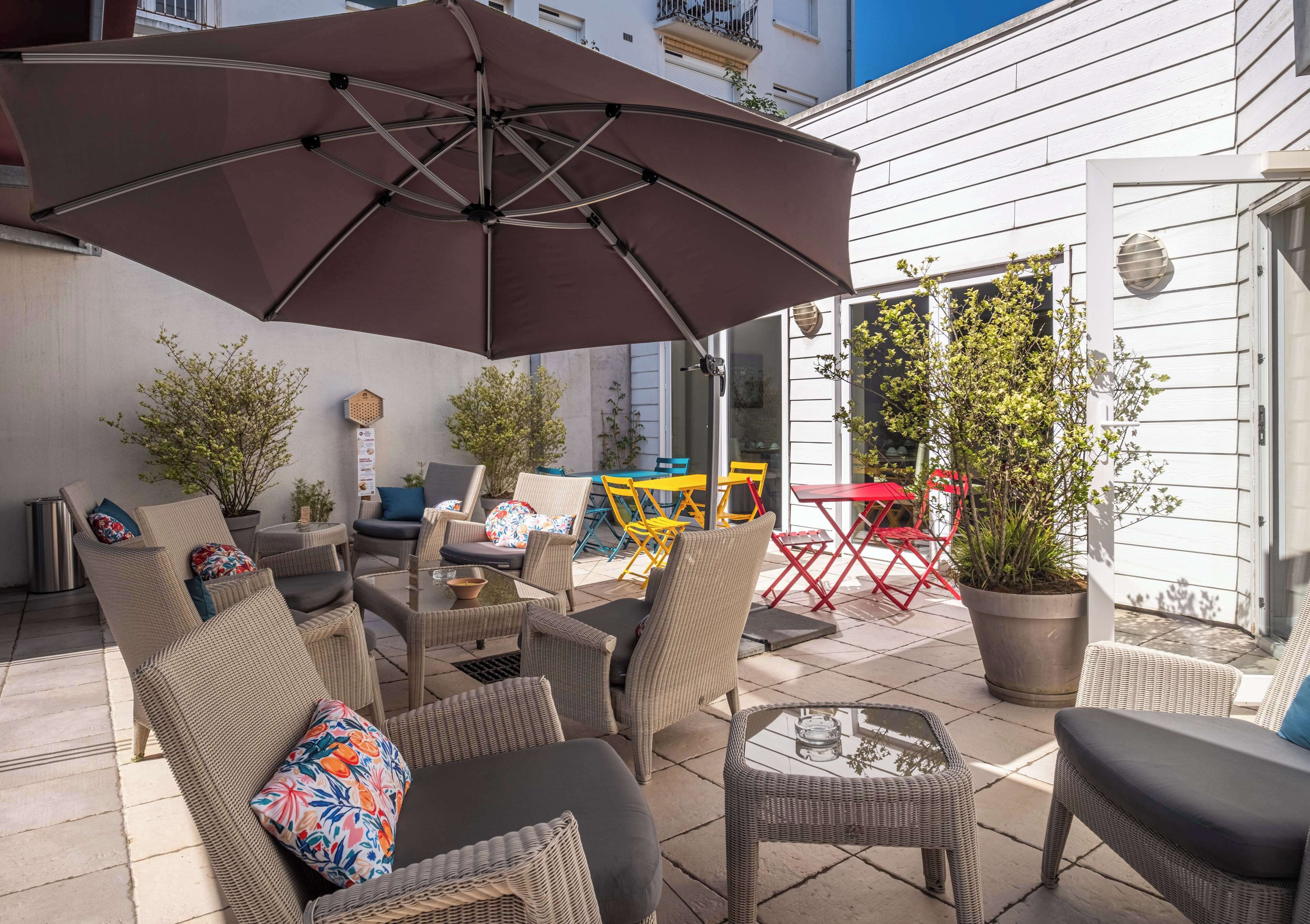 An outdoor patio with wicker furniture, a large umbrella, and potted plants.