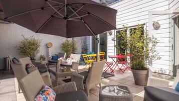 An outdoor patio with wicker furniture, a large umbrella, and potted plants.