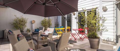 An outdoor patio with wicker furniture, a large umbrella, and potted plants.