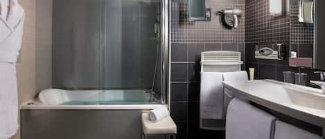 A modern bathroom with a glass-enclosed shower, a white bathtub, a vanity with a mirror, and a towel rack.