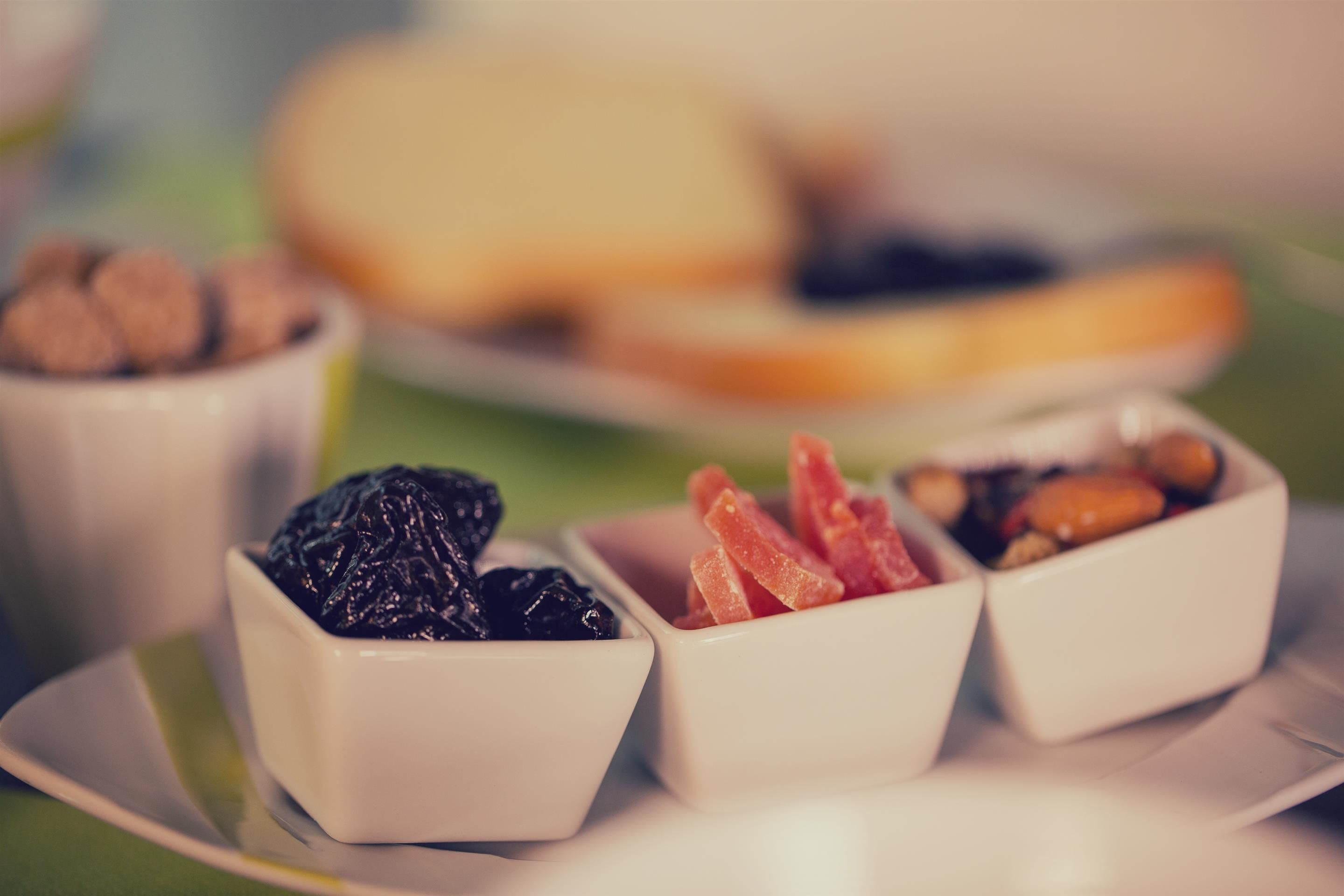 A plate with three small bowls containing different types of nuts and dried fruits.