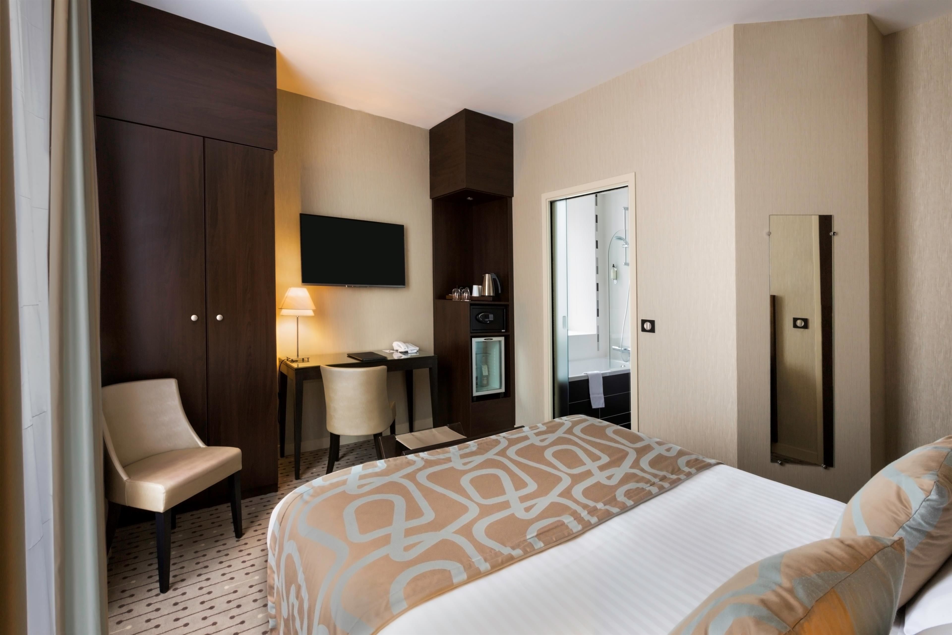 A hotel room with a bed, a desk, a chair, a TV, a mirror, and a wardrobe.