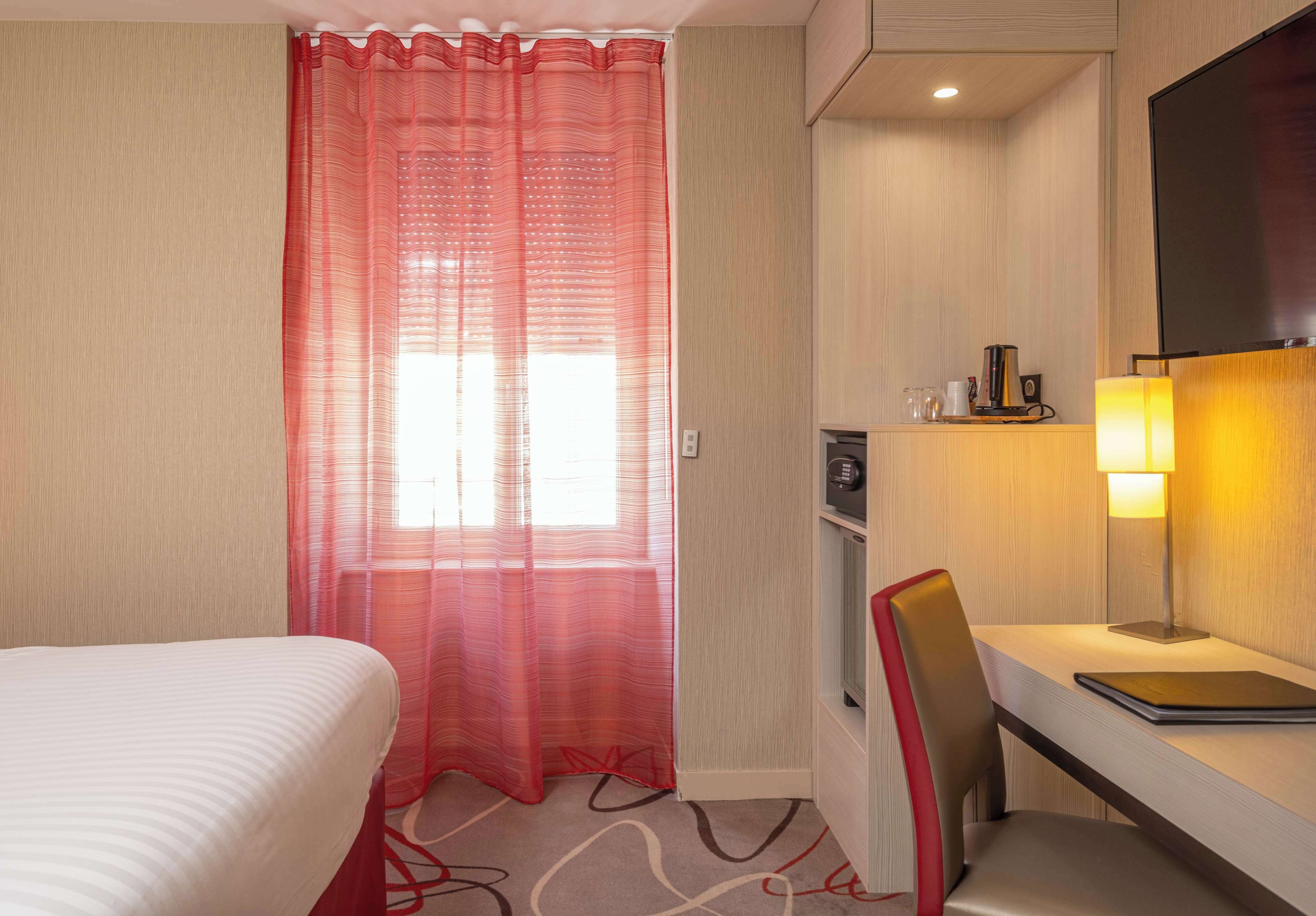 A hotel room with a bed, a desk with a chair, a TV, a lamp, and a shower area.