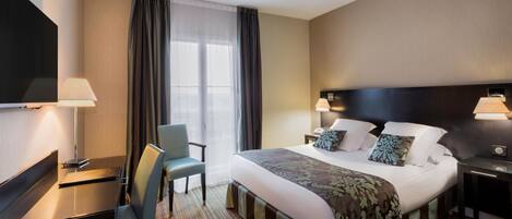 A hotel room with a bed, a desk, a chair, a TV, and a window with curtains.