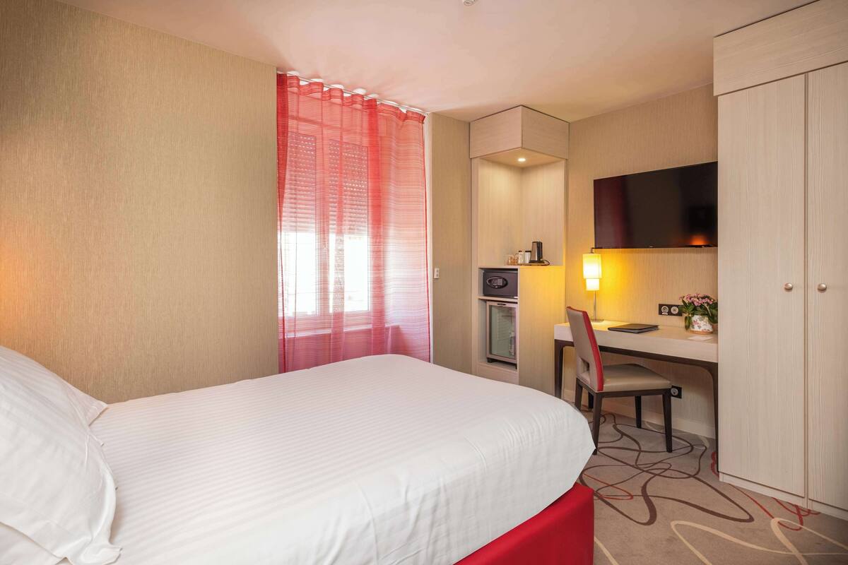 A hotel room with a bed, a desk, a chair, a television, and a wardrobe.