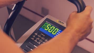 A treadmill with a digital display showing 50.00, a hand holding a handle, and a TV mounted on the wall displaying a cartoon.