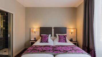 A double bed with a patterned bedspread, two bedside tables with lamps, and a shower area visible to the left.