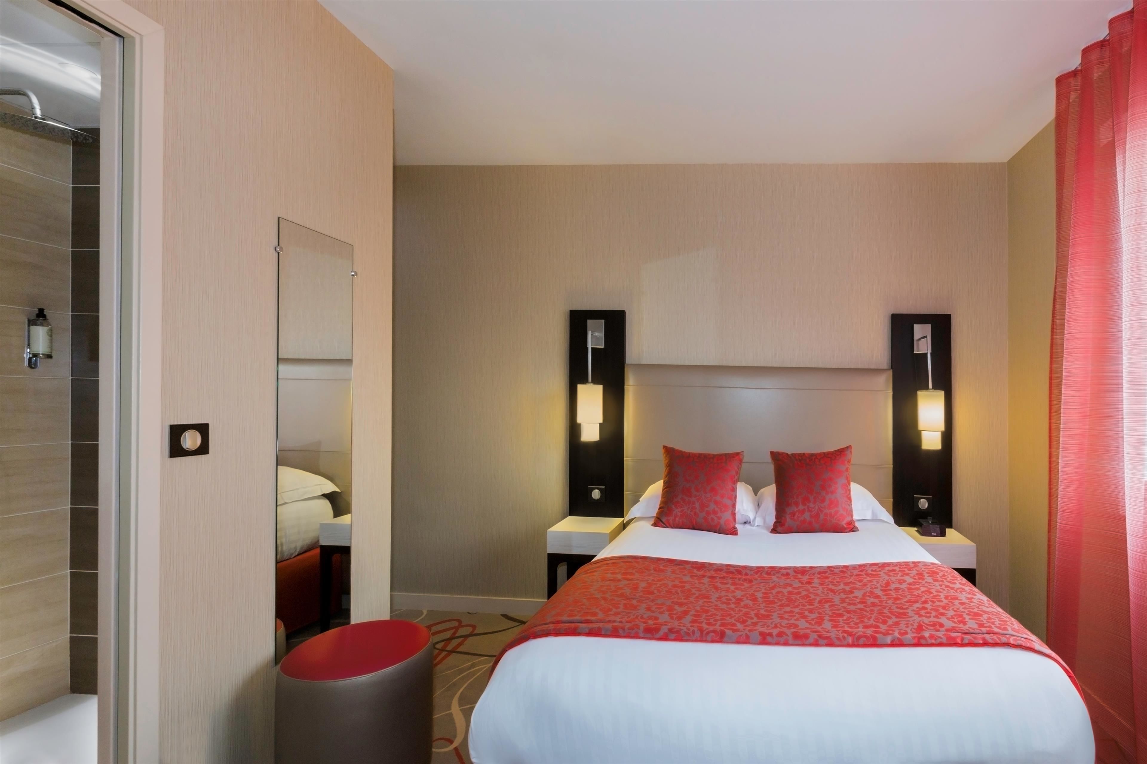 Habitación de hotel con cama, dos mesitas de noche, un tocador, un espejo y una cortina roja.
