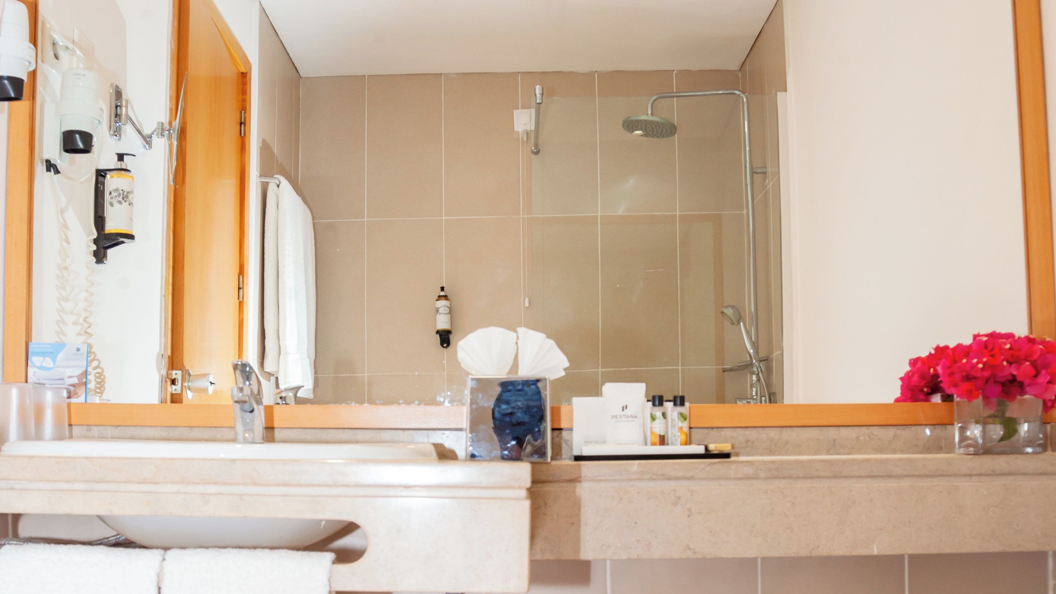 Un baño con lavamanos, espejo, ducha y artículos de aseo.