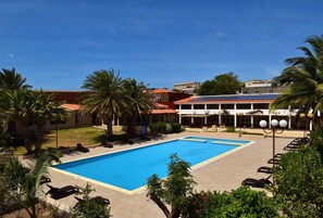 A swimming pool with lounge chairs, palm trees, and a building with a red roof.