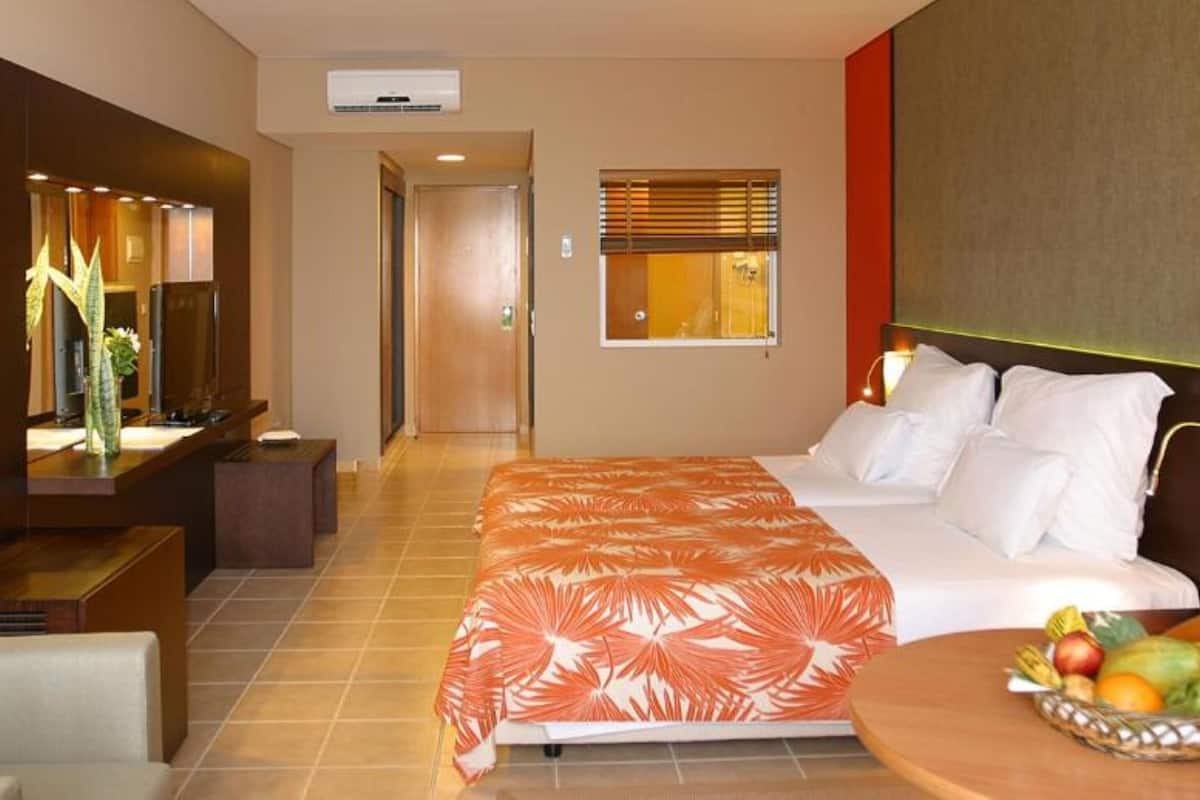 Hotelkamer met een bed, een bureau, een stoel, een schaal fruit en een raam met jaloezieën.