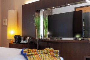 Une chambre d’hôtel équipée d’un lit, d’un téléviseur à écran plat, d’une machine à café et de deux plantes en pot.