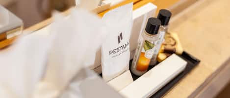 Un plateau contenant des articles de toilette, notamment un flacon de shampoing, un flacon d’après-shampoing et un sac en papier blanc orné du logo « Pestana Hotels & Resorts ».