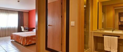 A hotel room with a bed, a desk, and a bathroom with a sink and mirror.