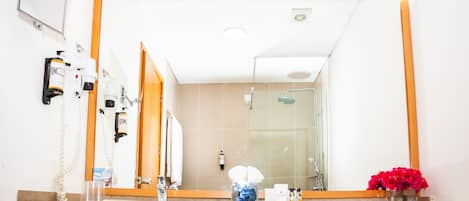 Un baño con un espejo grande, ducha y lavabo con un jarrón de flores.