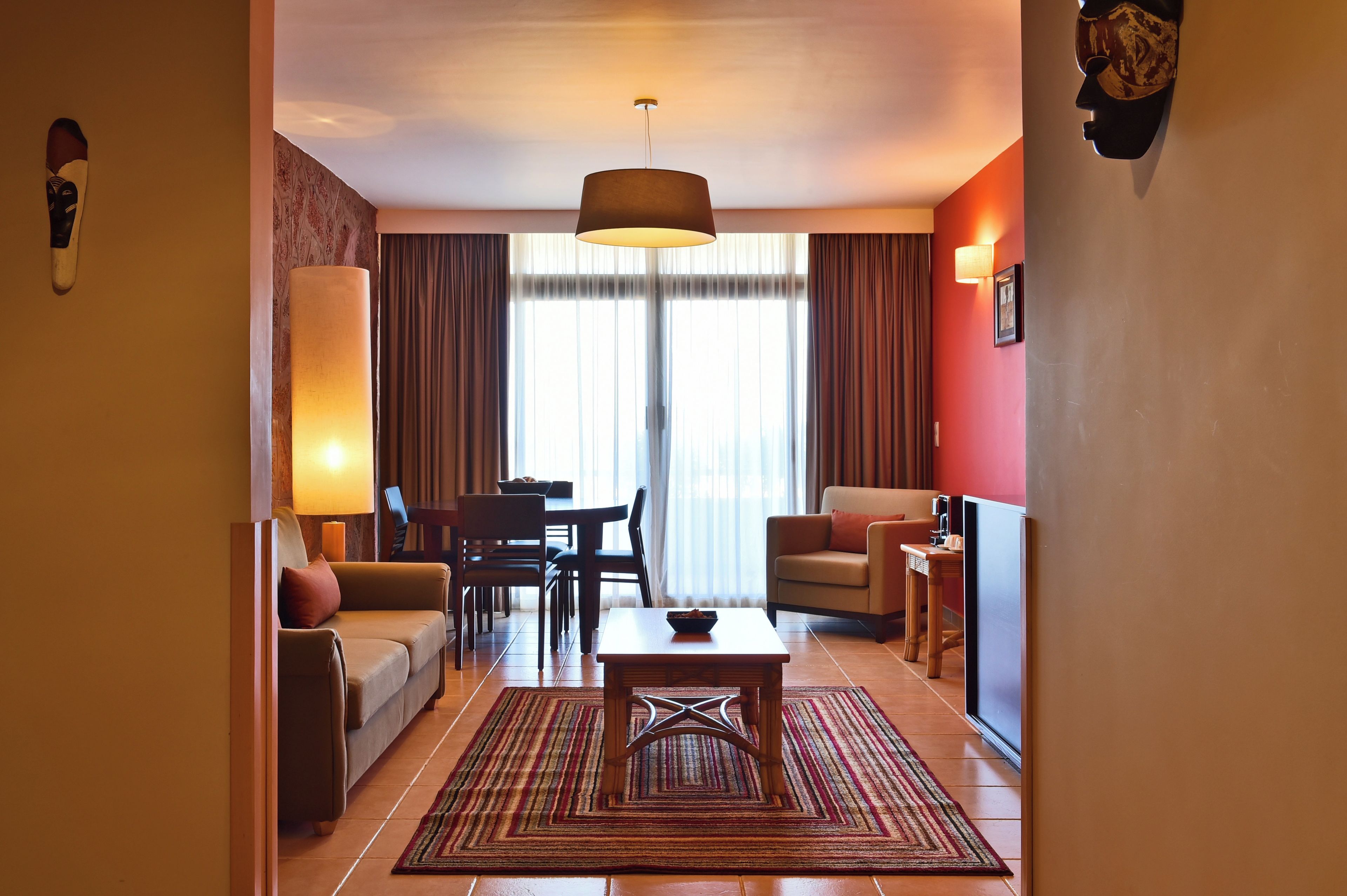 A hotel room with a dining area, a sofa, a TV, and a lamp.