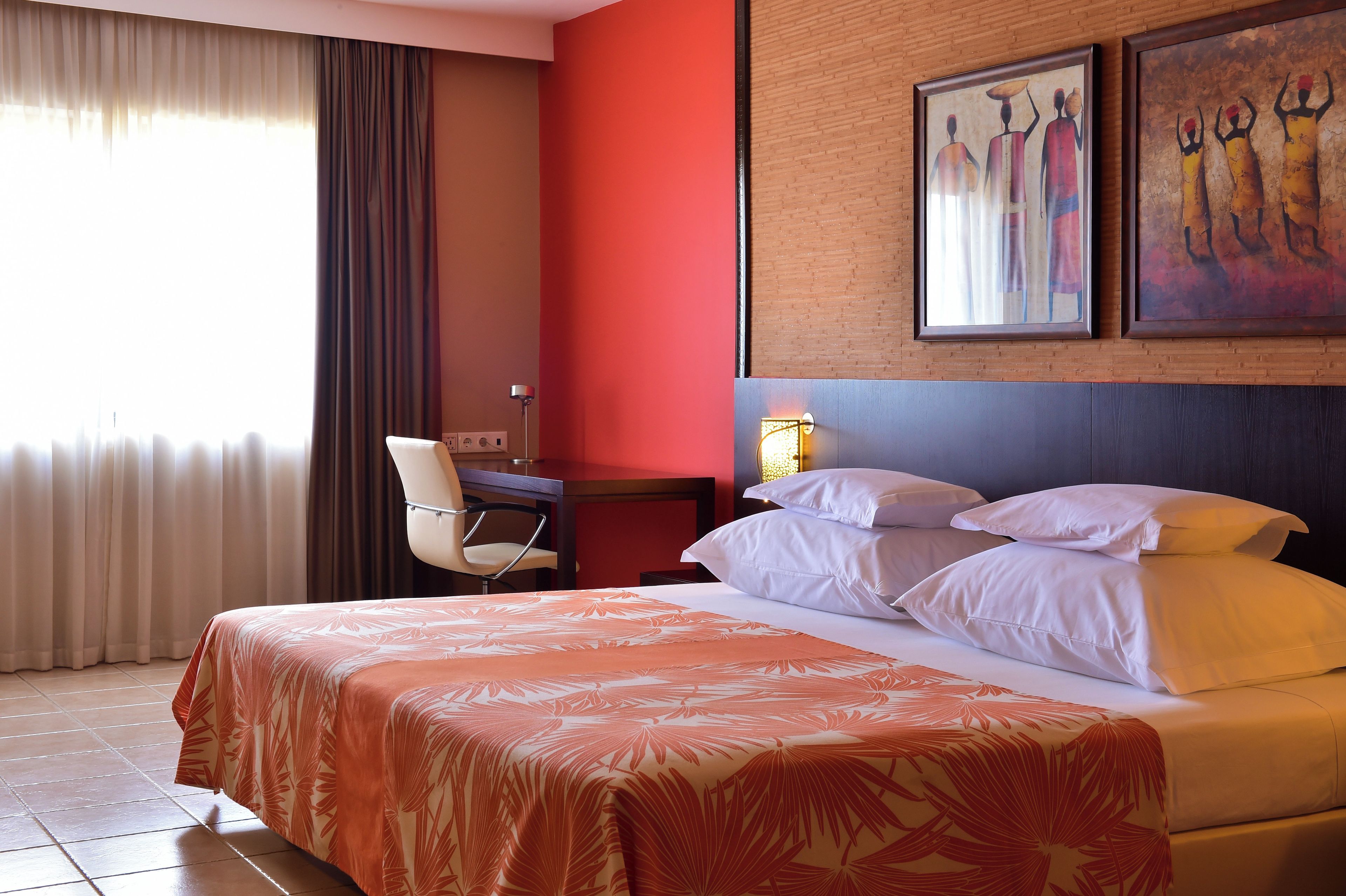 Una habitación de hotel con una cama, un escritorio, una silla y dos cuadros en la pared.