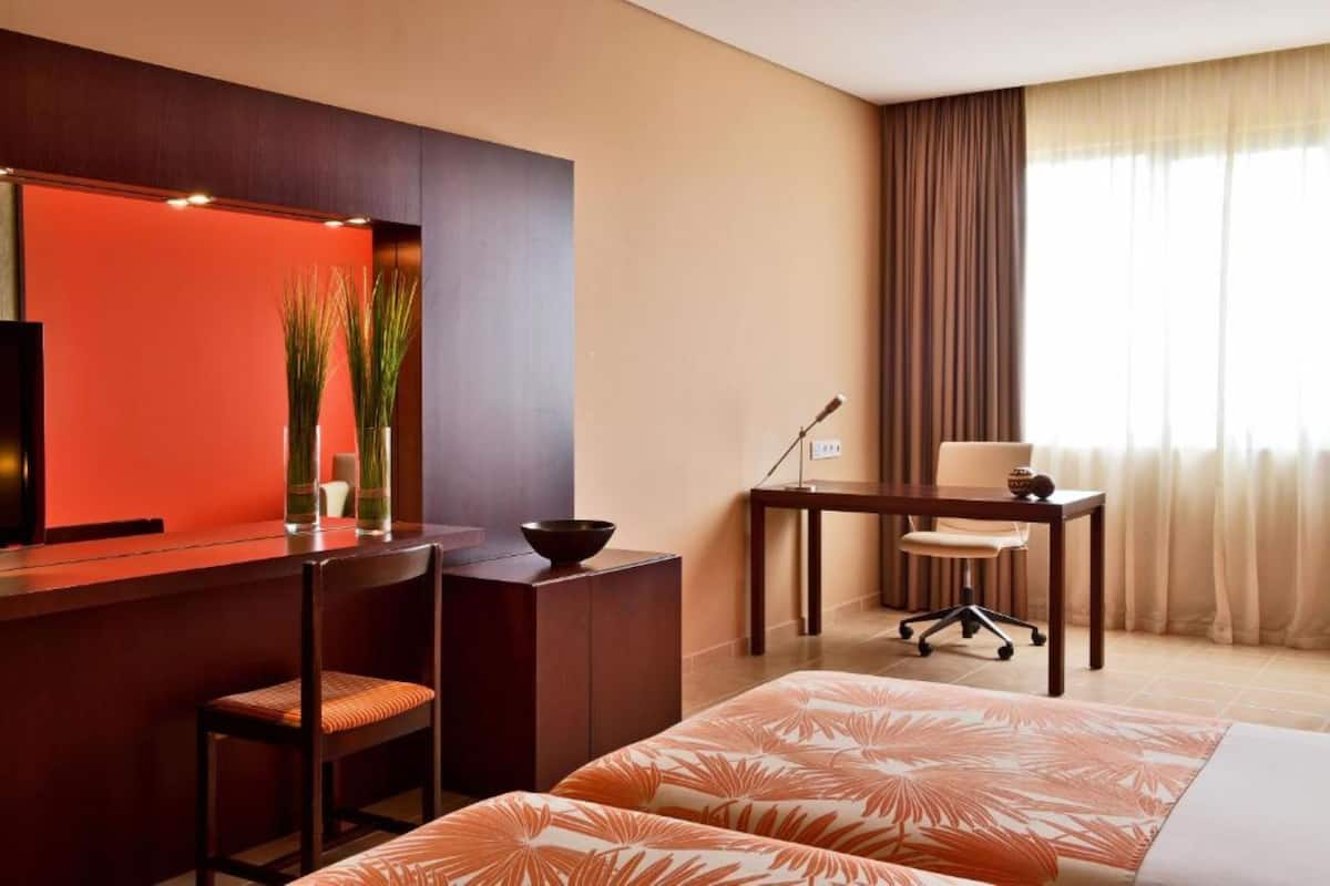 Een hotelkamer met een bed, een bureau met stoel, een televisie en een raam met gordijnen.