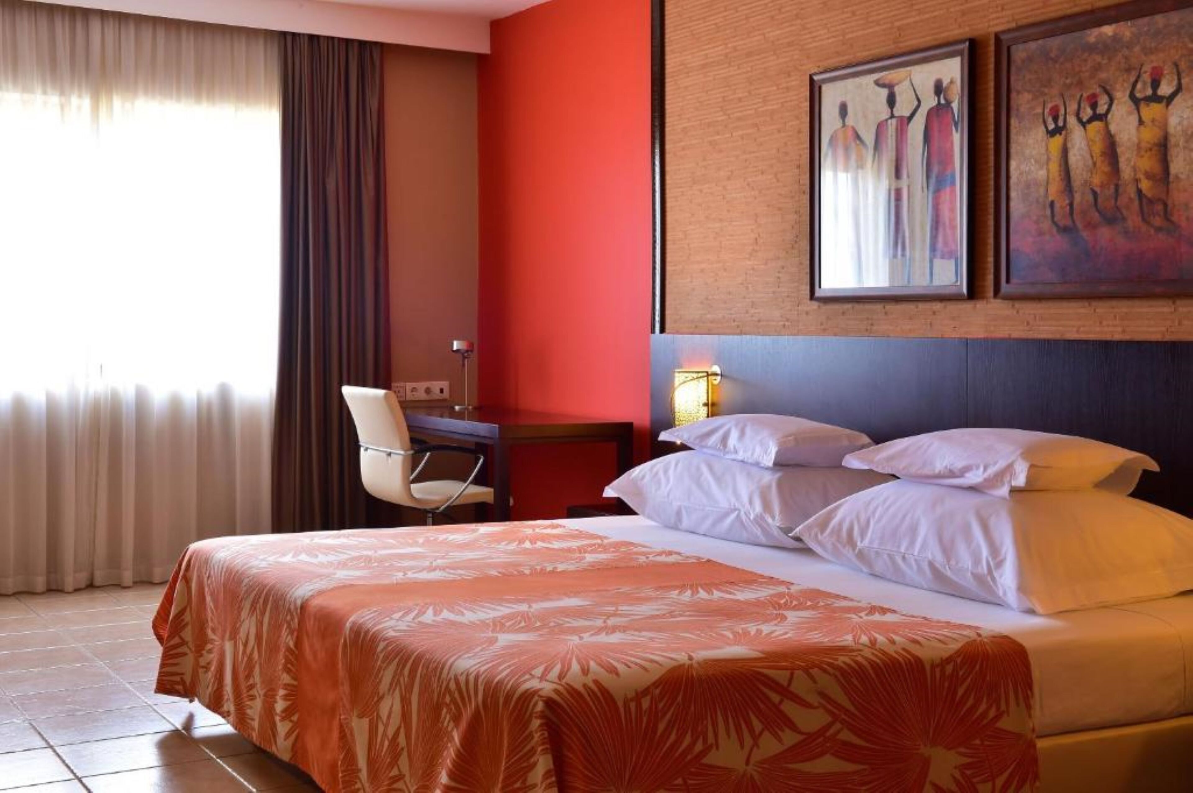 Habitación de hotel con cama, escritorio, una silla y dos cuadros en la pared.