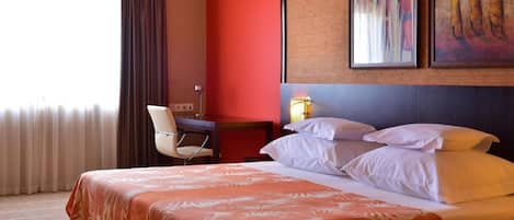 Habitación de hotel con cama, escritorio, una silla y dos cuadros en la pared.