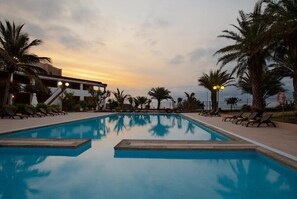 Ein Pool mit Liegestühlen und Palmen, umgeben von einem Gebäude mit Treppe und Beleuchtung.
