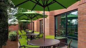 An outdoor patio area with round tables and green chairs, surrounded by brick walls and large windows. - SpringHill Suites by Marriott Portland Hillsboro (Hillsboro)
