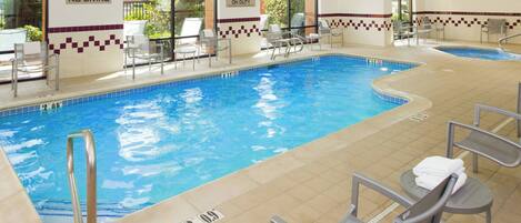 Una piscina interior con agua cristalina, rodeada de sillones de descanso y un suelo de baldosas.