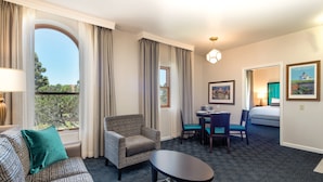 Habitación de hotel con sofá estampado, una mesita, un área de comedor con sillas y vistas a árboles por la ventana.