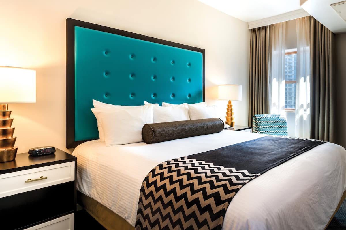 A hotel room with a large bed, a nightstand, a lamp, a TV, and a window with curtains.